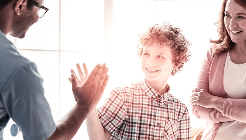 Care coordinator offering a boy a high five while his Mom watches and smiles