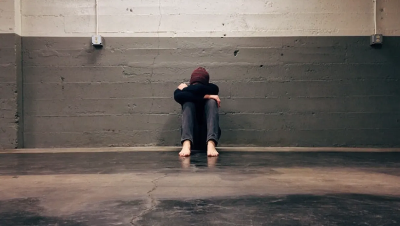 Distressed teen sitting on ground with their head resting on their arms.