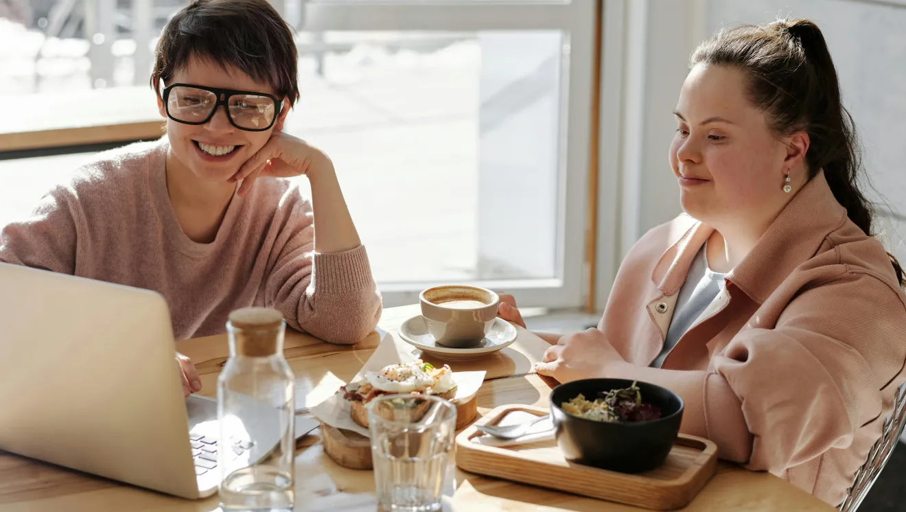 A caregiver assists a person with Down Syndrom while eating breakfast