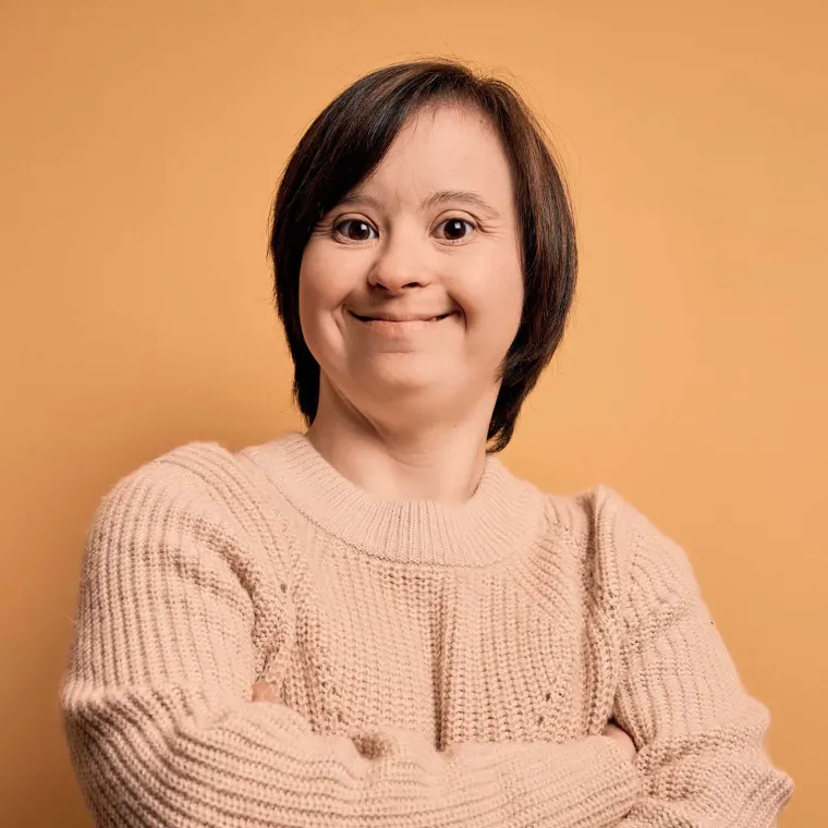 Person standing with their arms crossed, smiling, on an orange background.